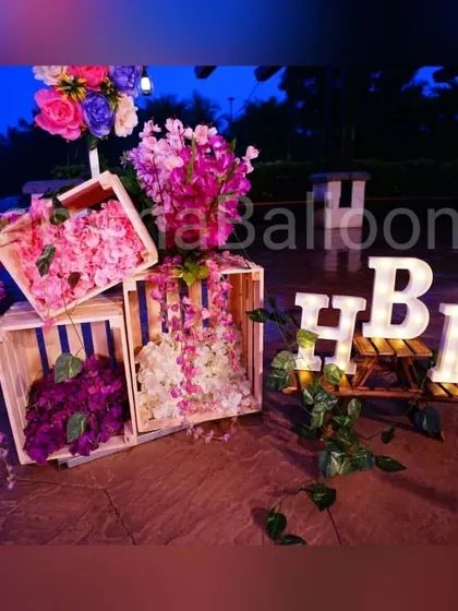 A rustic-chic decor detail featuring wooden crates filled with beautiful artificial flowers and light-up 'HBD' letters. This makes for a lovely corner decoration or photo prop.