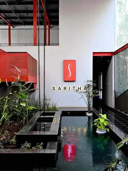 The indoor water feature at the Saritha Serene office reflects the red structural elements and signage. This thoughtful detail creates a sense of cohesion and adds a layer of visual complexity to the space.