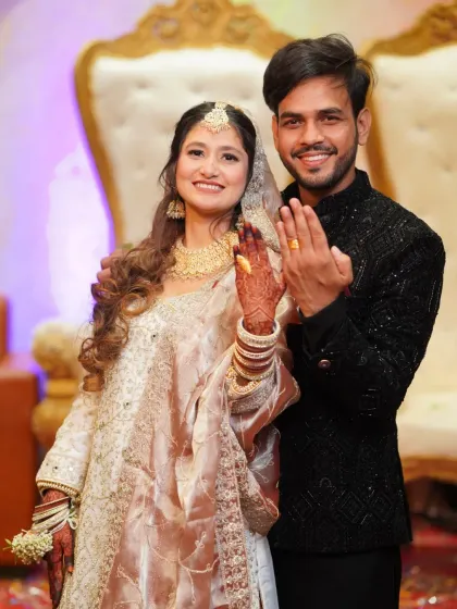 A beautiful portrait of the couple proudly displaying their engagement rings. The bride's intricate white and gold outfit and henna are stunningly detailed.
