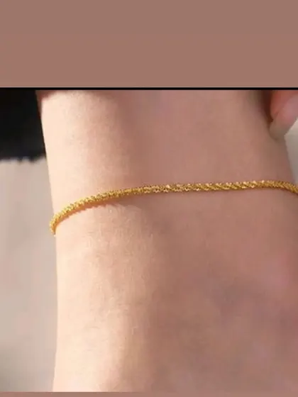 A delicate, sparkling gold-toned anklet worn to show its simple beauty. This piece is made from color-stable material.