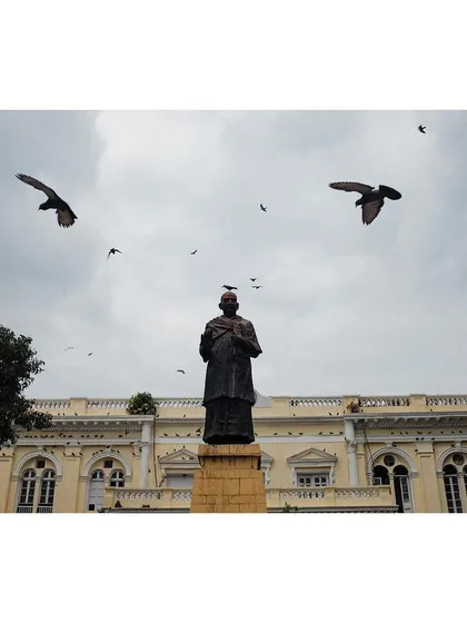 The statue of Indian independence activist Swami Shraddhanand in Delhi, with pigeons flying overhead. The shot captures a moment of history against a cloudy sky.