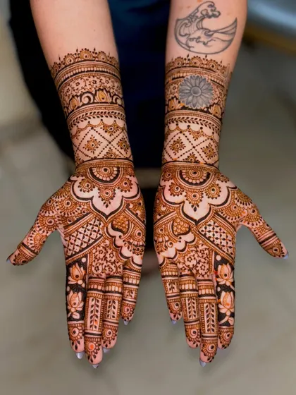This bridal design seamlessly incorporates the bride's existing tattoos into the mehendi artwork. The patterns flow around the tattoos, making them part of the overall design.