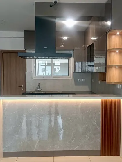 A completed kitchen with a breakfast bar, featuring a grey marble finish, fluted wood paneling, and under-counter lighting for a modern, sophisticated look.