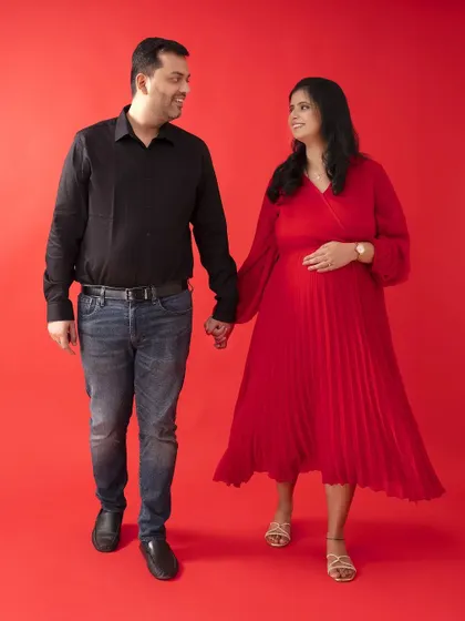 Walking into the journey of parenthood hand-in-hand. This dynamic pose against a red background captures the feeling of moving forward together.