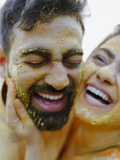 An intimate close-up of the couple laughing together, their faces smeared with turmeric in a moment of shared fun.