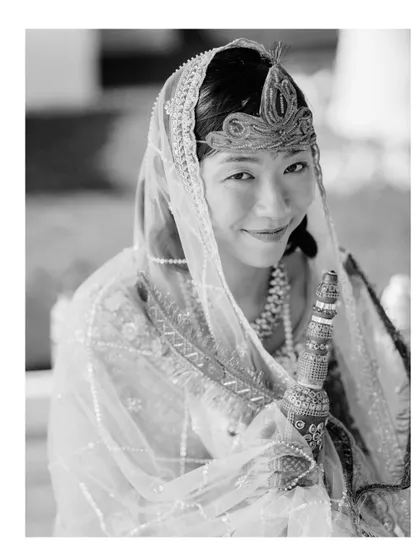 A classic black and white bridal portrait. The bride's gentle smile and traditional attire are captured with timeless elegance.