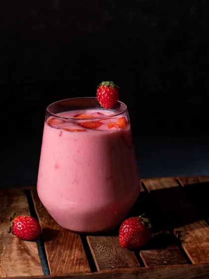 A simple, elegant shot of a strawberry milkshake against a dark, moody background. The lighting highlights the creamy texture and rich pink color of the drink.