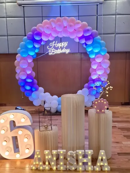 A full view of the 6th birthday party decoration, showing the arrangement of the balloon ring, marquee letters, and plinths on the wooden floor.