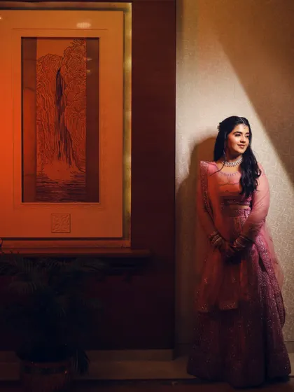 The bride leans against a wall, bathed in a soft, directional light. This artistic portrait highlights her thoughtful expression and the beautiful details of her outfit.