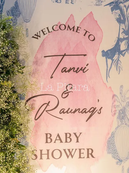 A welcome sign for Tanvi and Raunaq's Baby Shower, featuring a soft pink watercolor splash against a chic 'Baby Dior' patterned background.
