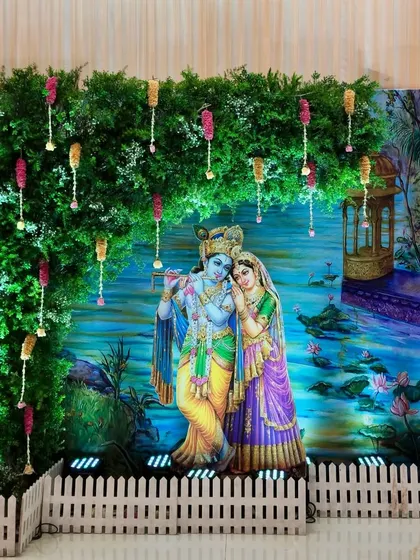 A Radha-Krishna themed photo corner we created for a baby shower at Hiravati Hall. The divine couple is set against a lush green foliage wall with delicate hanging floral tassels, creating a perfect photo opportunity.