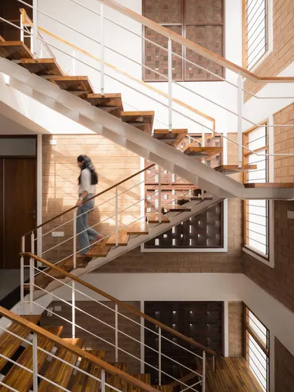 A resident ascends the open-tread staircase, which allows light to filter through the different levels of the home. The combination of wood, steel, and exposed brick creates a rich material palette.