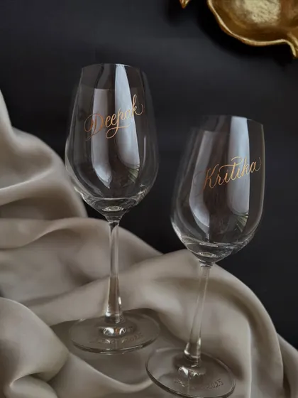 A set of personalized wine glasses for a couple, engraved with their names in a flowing script and the date on the base. These make for a beautiful and timeless wedding or anniversary gift.