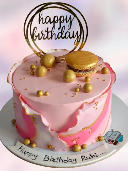 A beautiful fault line cake in shades of pink with elegant gold accents. Topped with golden spheres, a macaron, and a "Happy Birthday" topper, this design is perfect for a stylish celebration.