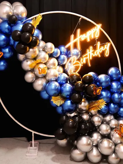 A modern and stylish balloon arch on a white ring frame, using metallic blue, black, and silver balloons with gold butterfly accents.