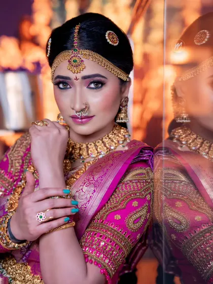 A powerful and confident pose from a bride in her full wedding attire. The makeup is bold and defined, designed to match the grandeur of the occasion and the heavy gold jewellery.