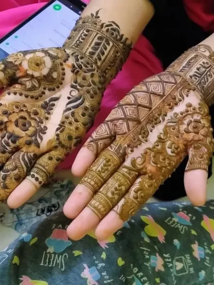 Two hands showcasing intricate bridal-level detail, with geometric patterns on one and floral on the other.