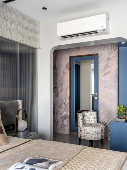 An arched entryway leads to the walk-in closet in this master bedroom. The feather-print wallpaper and floral chair add a touch of softness and personality.