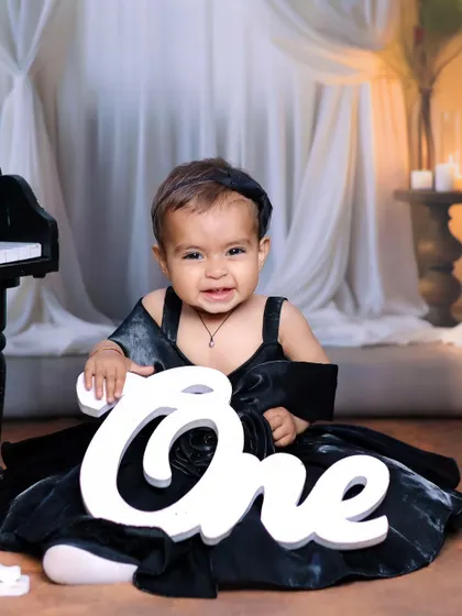 A happy one-year-old girl holding a 'One' sign during her elegant piano-themed birthday shoot.