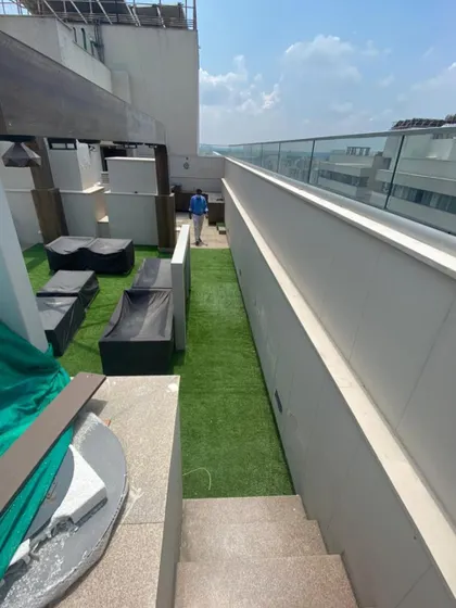 A long view of a narrow terrace space transformed with a strip of artificial grass, providing a green walkway alongside modern outdoor lounge furniture.