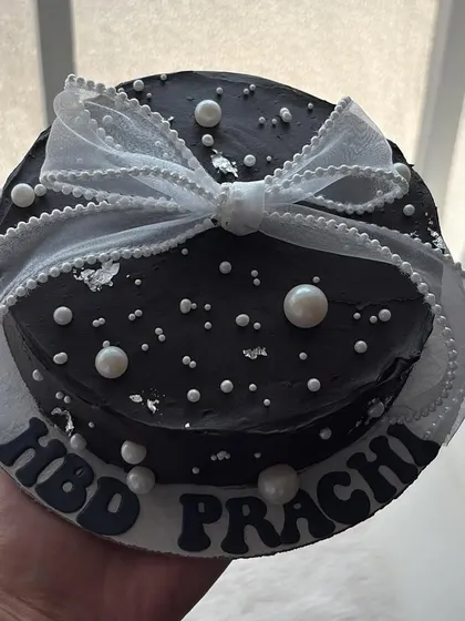 A glamorous mini cake in dark chocolate, decorated with edible pearls, silver leaf, and a beautiful white ribbon.
