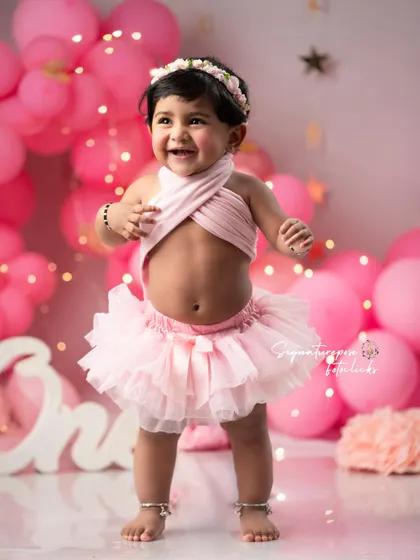 Standing tall and proud on her first birthday. This portrait captures a key milestone, the ability to stand, amidst the fun and festive setup of her cake smash session.