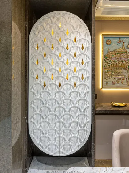 This elegant, space-saving mandir is concealed within a custom Corian cabinet. The oval-shaped doors feature a beautiful carved pattern with golden inlays that glow when the mandir is lit from within.