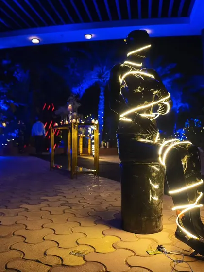 An artistic installation of a mannequin wrapped in LED strip lights, adding a cool, futuristic vibe to the event's entrance pathway.