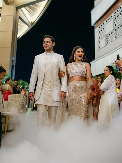 The grand entrance of the couple, walking through a cloud of low fog. The bride's excited expression and their linked arms signal the start of their celebration in style.