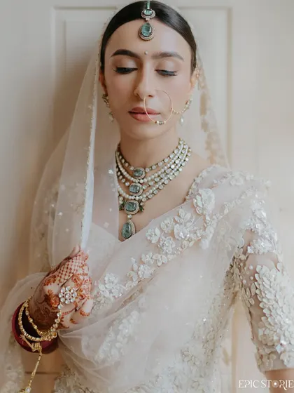 A close-up portrait focusing on the bride's serene expression and exquisite jewelry. This shot highlights the delicate details that complete the bridal look, from the nath to the layered necklace.