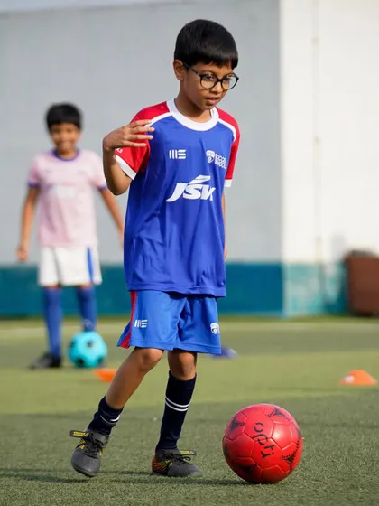 A young player with glasses dribbles with confidence. We create an inclusive environment where every child can develop their skills and passion for football.
