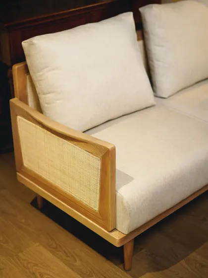 A close-up of our cane-panel sofa, showing the seamless integration of the handwoven cane into the light-toned wood frame. The neutral fabric makes it a versatile piece for any decor.