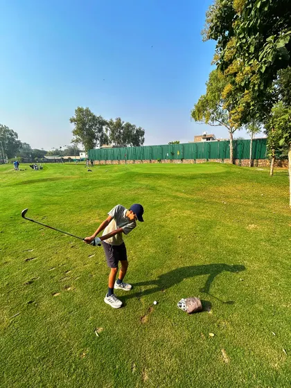 A young golfer practices his chipping under the bright sun, a perfect day for the grind.