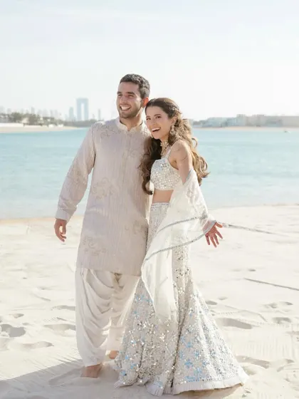 A sunny beach portrait of Alya and Shivaan. Their happy, relaxed smiles and the beautiful seaside location create a perfect destination wedding portrait.