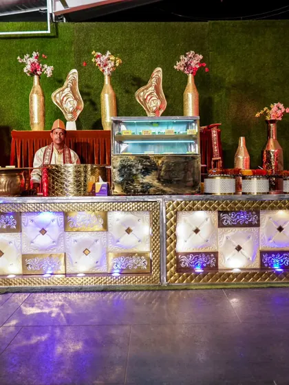 An elaborate white and gold catering counter, complete with a refrigerated display for desserts and traditional staff attire.