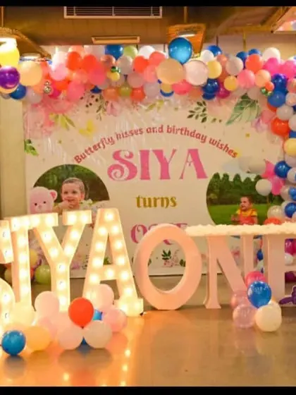A vibrant butterfly-themed stage for Siya's first birthday. The mix of a custom printed backdrop, balloon garland, and light-up letters creates a complete and festive look.