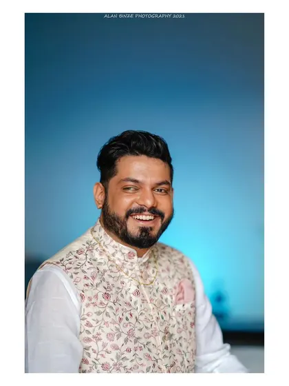 A portrait of a groom, looking sharp and happy. The soft blue background and his warm smile make this a great shot for a wedding album.