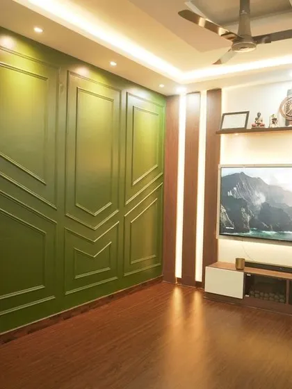 We designed this living room with a feature wall of royal green paint and decorative beading, creating a sense of refined elegance. The custom TV unit with wooden louvers and a floating console completes this sophisticated space.