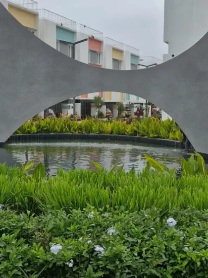 The same water feature by day, showing how the concrete sculpture acts as a modern art piece within the landscape. The surrounding greenery and calm water provide a tranquil atmosphere in this residential development.