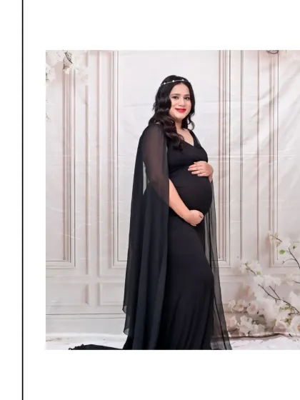 A full-length portrait of the same elegant black gown. The delicate headband adds a touch of sparkle, and the pose is confident and graceful. This is a perfect example of a modern, glamorous maternity look.