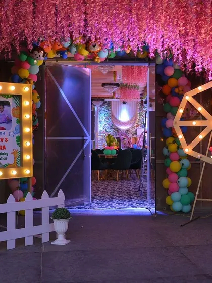 An elaborate entrance for a jungle-themed party. The decor includes a pink floral ceiling, a lighted welcome frame, and props like a Ferris wheel and animal cutouts.