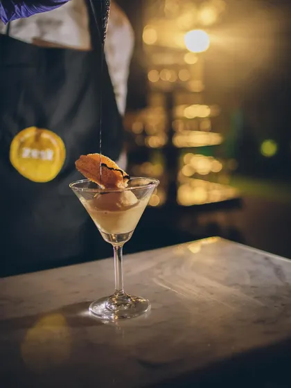 A chef pours a finishing sauce over an ice cream dessert in a martini glass.