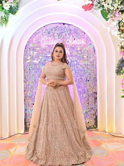 A full shot of a client looking radiant in the champagne gold lehenga against a decorative wall.