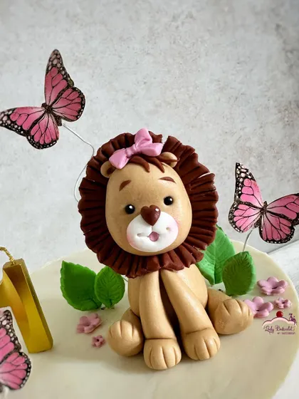 The star of the show! A close-up of the sweet, hand-sculpted lioness topper with her pink bow and butterfly friends.