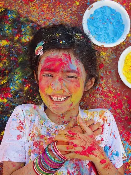 The pure joy of Holi! This little girl is having the best time, covered in bright colors with a huge, happy smile on her face. This is what festive fun looks like.