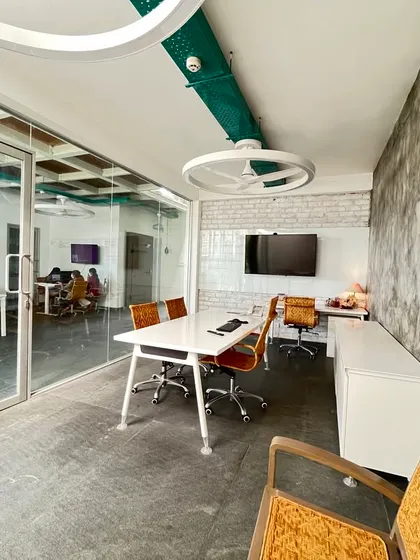 A private cabin in our studio, showcasing a minimalist aesthetic with a mix of textures. The concrete-finish wall contrasts with the white brick and glass partition, creating a sophisticated and modern meeting space.