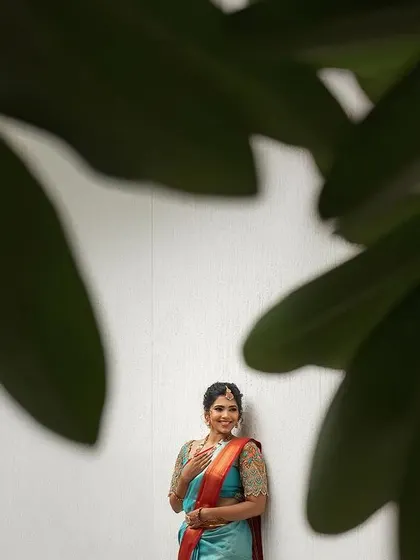A minimalist portrait of a bride framed by large green leaves. The simple composition draws all attention to her happy expression and colorful saree.