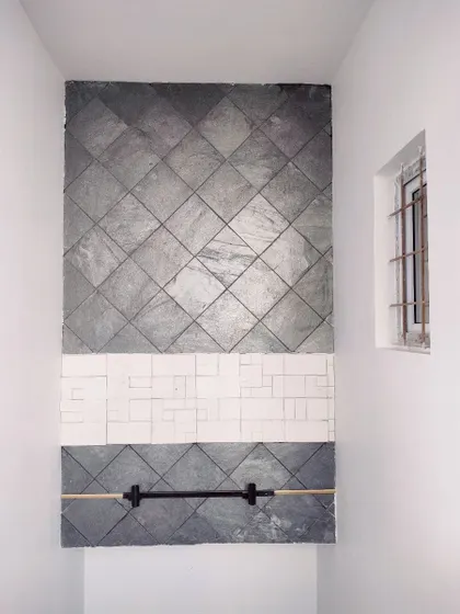 This on-site image shows a unique wall cladding design for a staircase wall. The feature uses a combination of diamond-patterned grey slate tiles and a central band of white textured tiles for a striking effect.