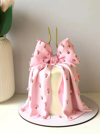 A chic and fashionable bow cake. The buttercream is draped and folded to look like fabric, with tiny hand-piped flowers for a delicate finish.