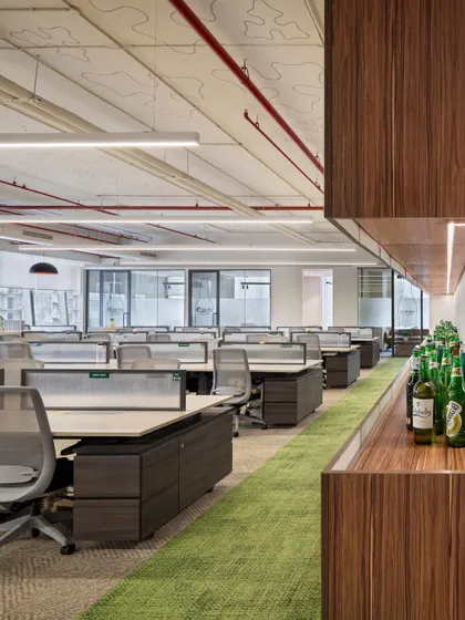 This view of an open-plan office shows our focus on creating a vibrant yet organized environment. The green carpet path not only adds a pop of color but also defines a clear circulation route, while the exposed ceiling adds an industrial-chic aesthetic.